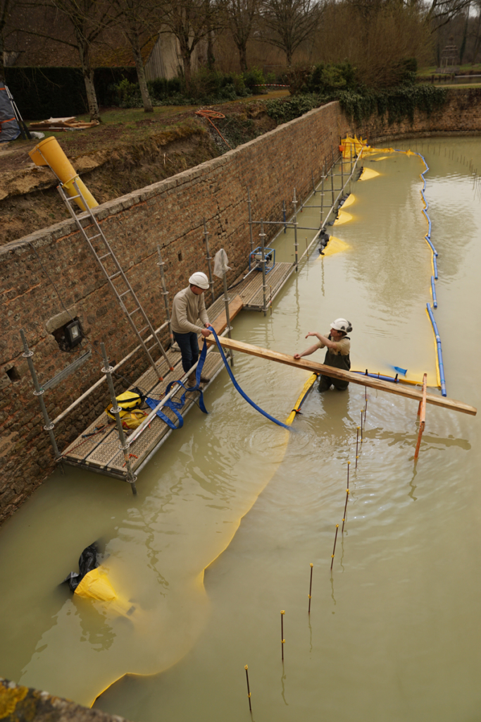 Tuyau d’évacuation de pompe franchissant la crête d’un batardeau souple dans les douves du château